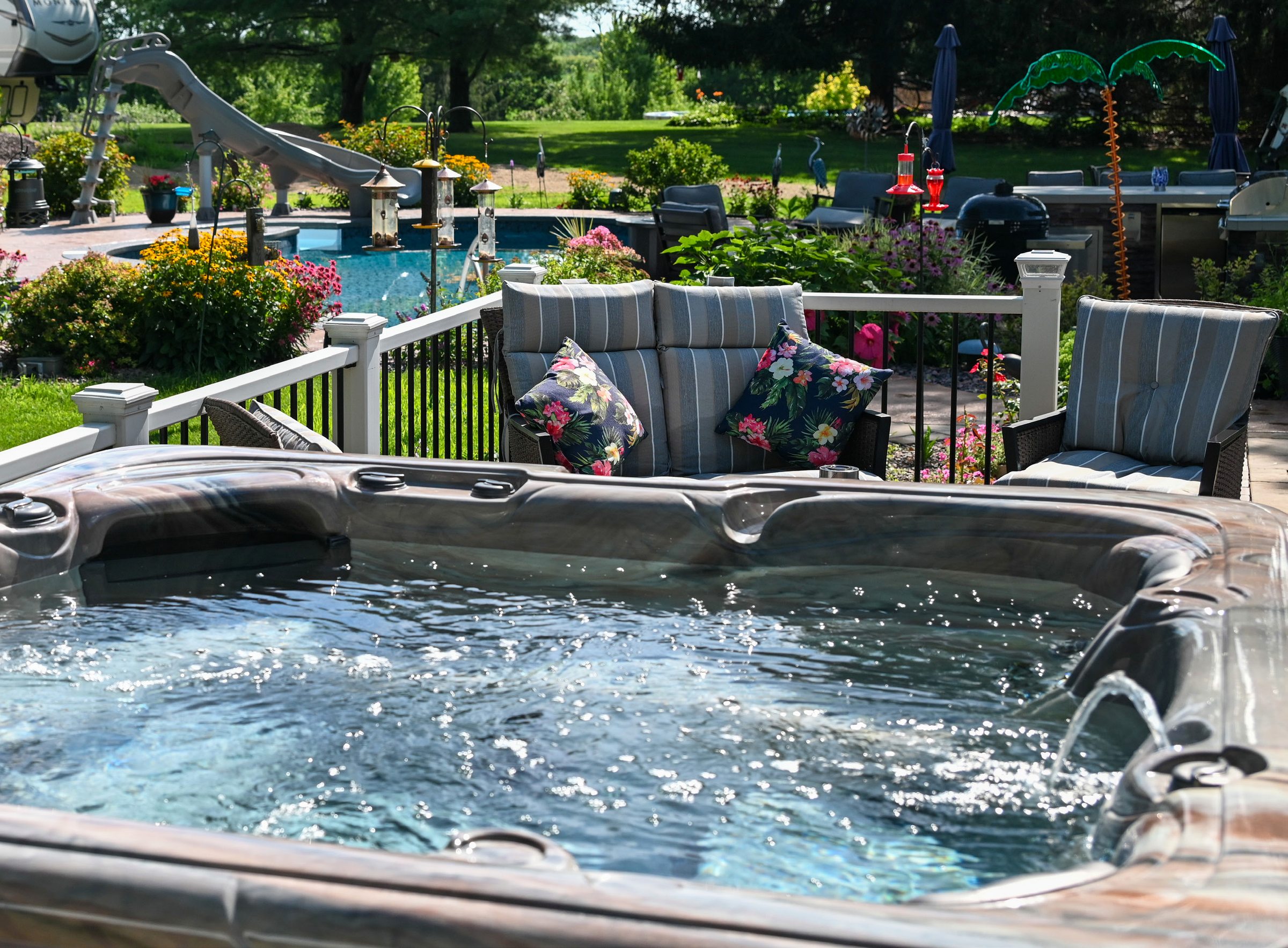 A Garden Leisure hot tub on a patio in a landscaped backyard, with a pool and seating beyond