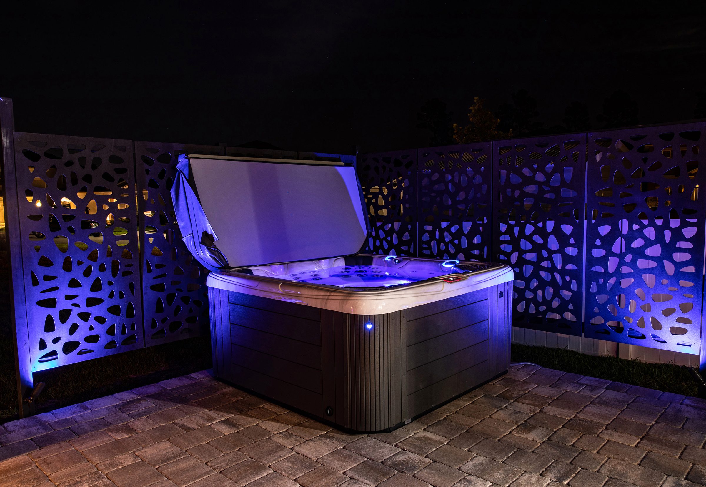 A Garden Leisure hot tub lit at night with the cover open, privacy screens behind